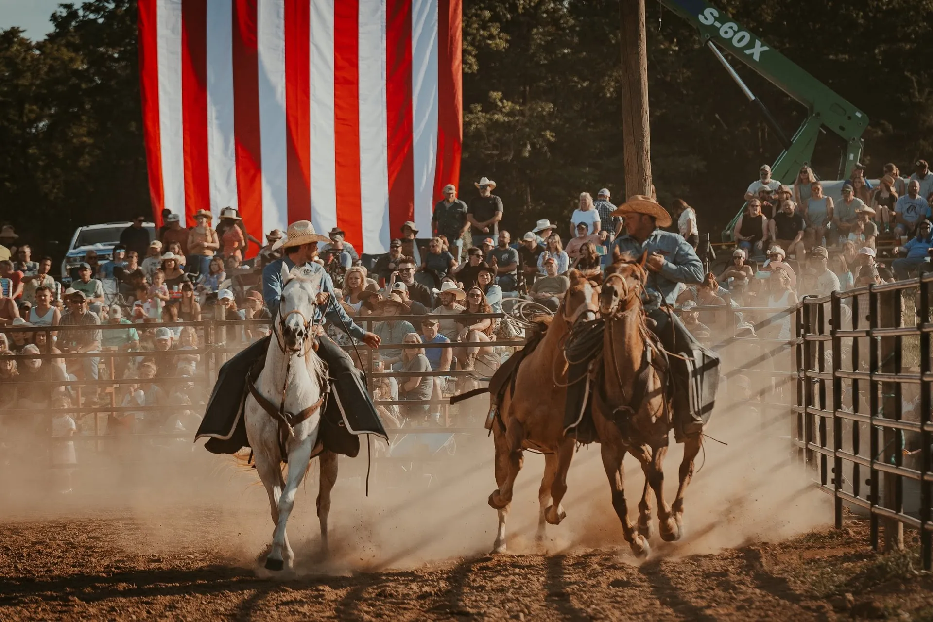 Horse riders enter the arena beneath a large American flag and in front of the crowd